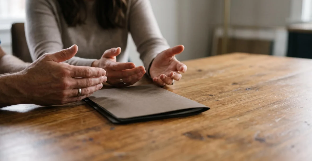 Mains de deux membres d'une famille posées côte à côte sur une table en bois, symbolisant un dialogue apaisé autour d'une succession