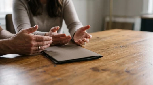 Mains de deux membres d'une famille posées côte à côte sur une table en bois, symbolisant un dialogue apaisé autour d'une succession